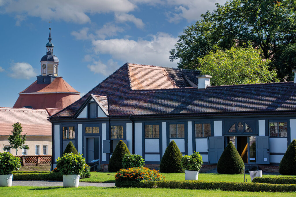 Bâtiment à colombages noirs et blancs, toit rouge à deux pans et pignon transversal, haies de buis au premier plan, parc du château d’Oranienbaum